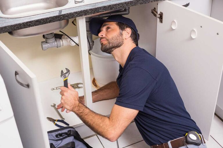 A homeowner examines wastewater backing up near a basement floor drain while nearby plumbing fixtures remain visible.