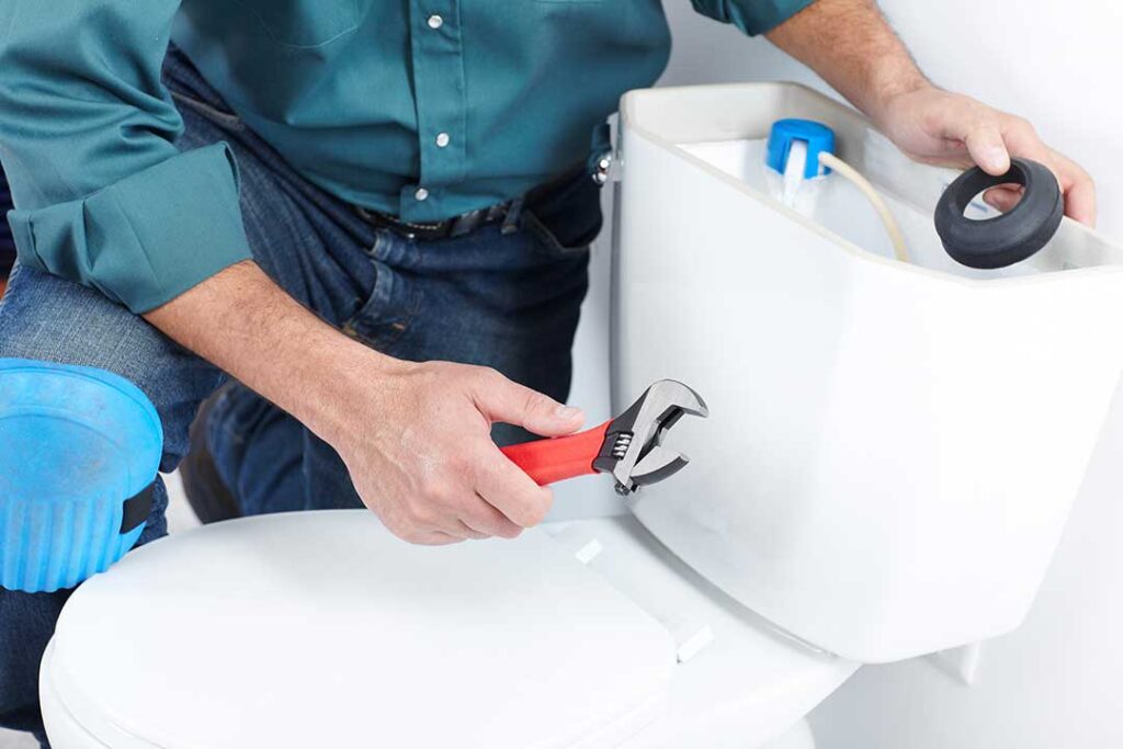Hands inspect a toilet tank with the lid removed, showing the flapper, float, refill tube, and water level.